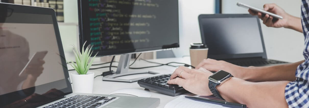 Ein Mensch sitz vor drei Bildschirmen und tippt etwas auf der Tastatur